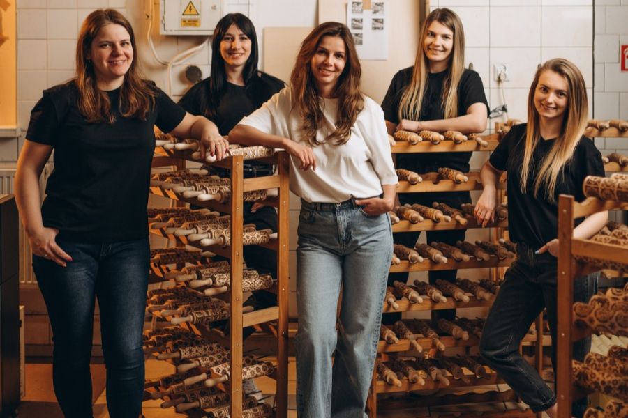 The Pastrymade team, five women, standing between racks of engraved rolling pins in the workshop